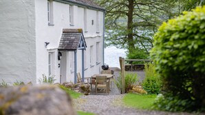 A white building with a stone roof, a wooden table and chairs, and a gravel path leading to a body of water. - Lakeshore cottage with Hot Tub - Hullet Hall (Graythwaite)