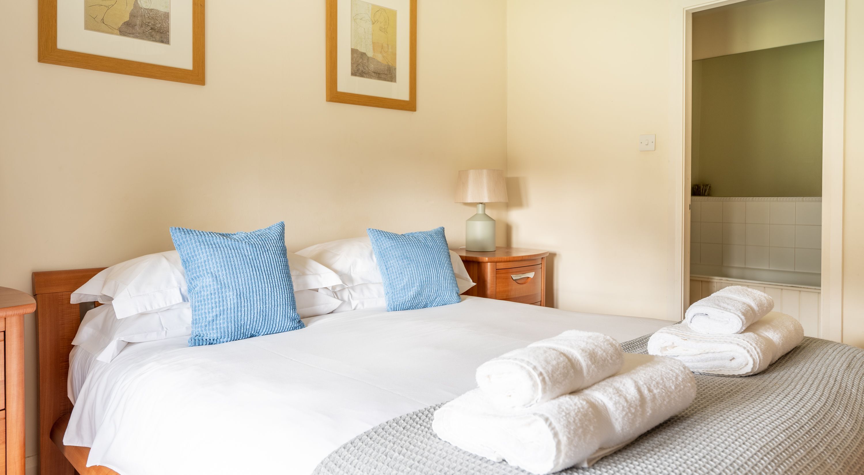 A hotel room with a bed, two pillows, a bedside table with a lamp, and a bathroom visible through an open door.