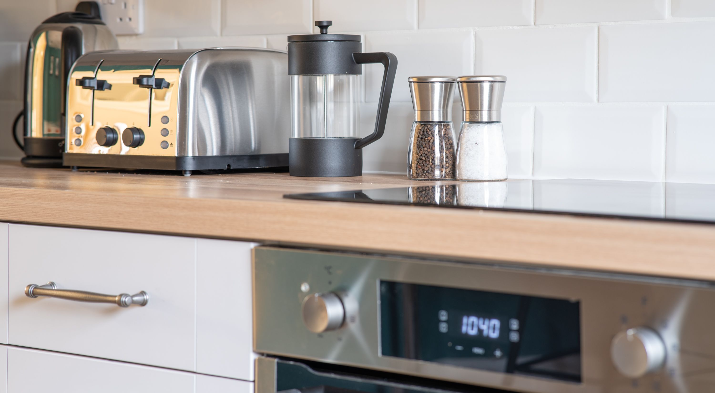 A kitchen with a coffee maker, salt and pepper shakers, a toaster, and an oven with a digital clock displaying 1040.