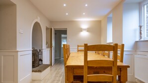 A dining area with a long wooden table and chairs, a fireplace, and recessed ceiling lights. - Fishery Views - Keepers Cottage (Graythwaite)
