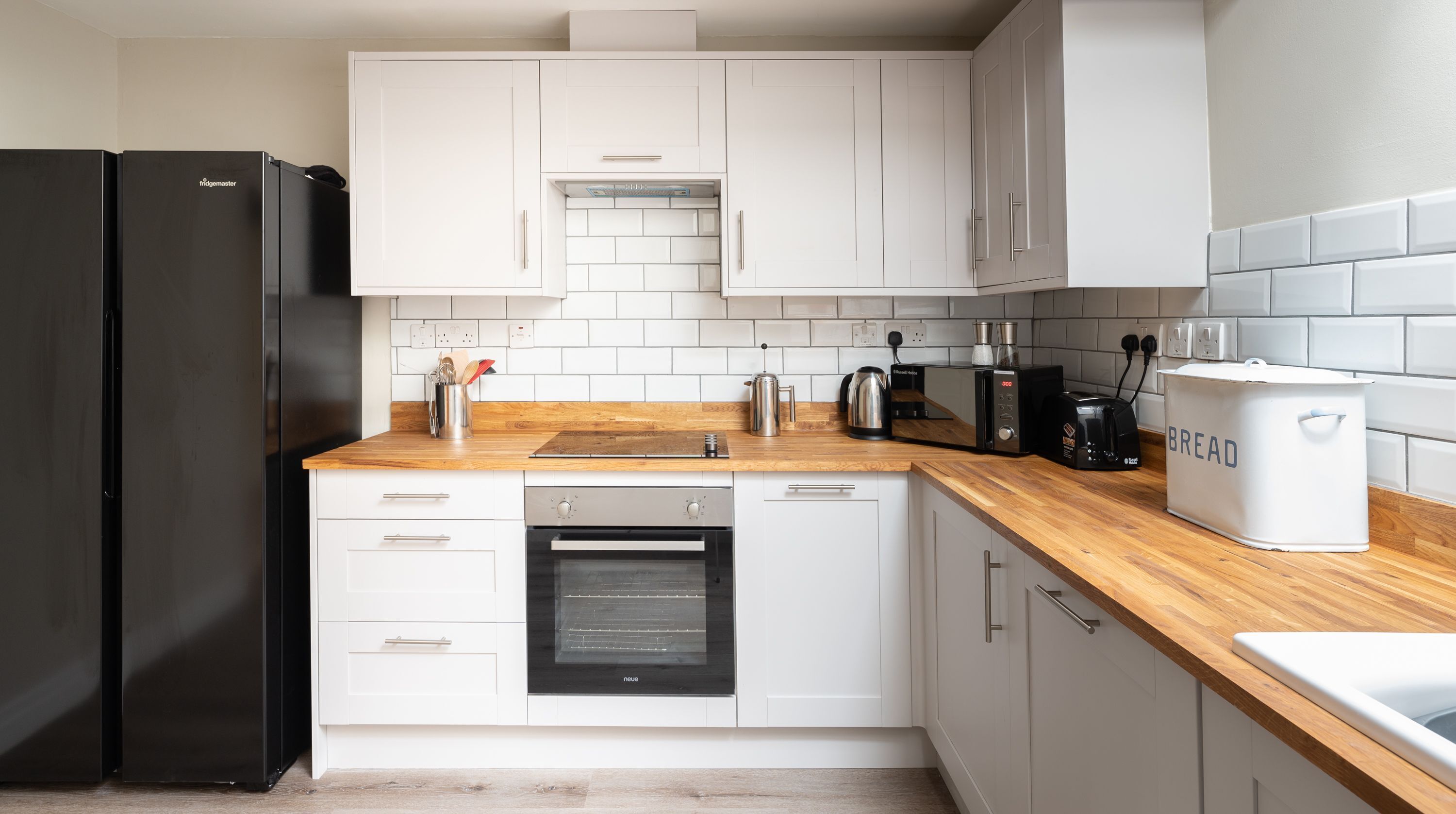 A modern kitchen with white cabinets, a black refrigerator, a built-in oven, a coffee maker, and a bread box.