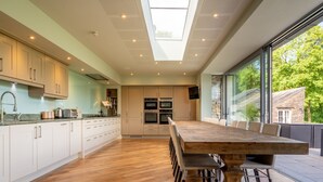 Een moderne keuken met een grote houten eettafel, witte kasten en een dakraam.