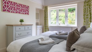 A bedroom with two beds, a dresser, a window with curtains, and a wall-mounted artwork.