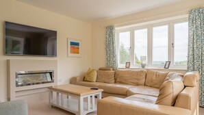 A living room with a beige leather sofa, a flat-screen TV mounted on the wall, a small wooden coffee table, and a fireplace.