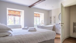 Ein Schlafzimmer mit einem großen Bett, zwei Fenstern mit gemusterten Vorhängen, einer Badewanne und einem weißen Kleiderschrank.