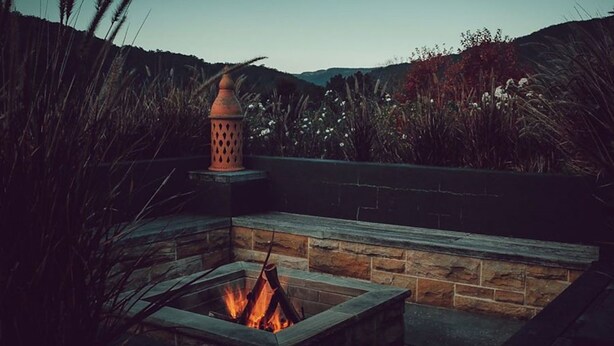 A stone fire pit with a lantern, surrounded by tall grasses and hills in the background. - Lastover Cottage - Kangaroo Valley (Wattamolla)