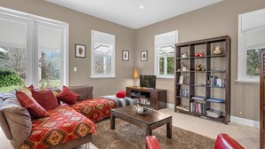 A living room with a sofa, a coffee table, a bookshelf, and a TV. - Lastover Cottage - Kangaroo Valley (Wattamolla)