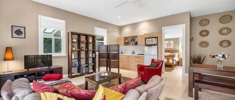 A modern living room with a sofa, TV, bookshelf, and a kitchen in the background.