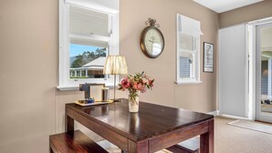 A room with a wooden table, a lamp, a vase with flowers, and a wall clock. - Lastover Cottage - Kangaroo Valley (Wattamolla)