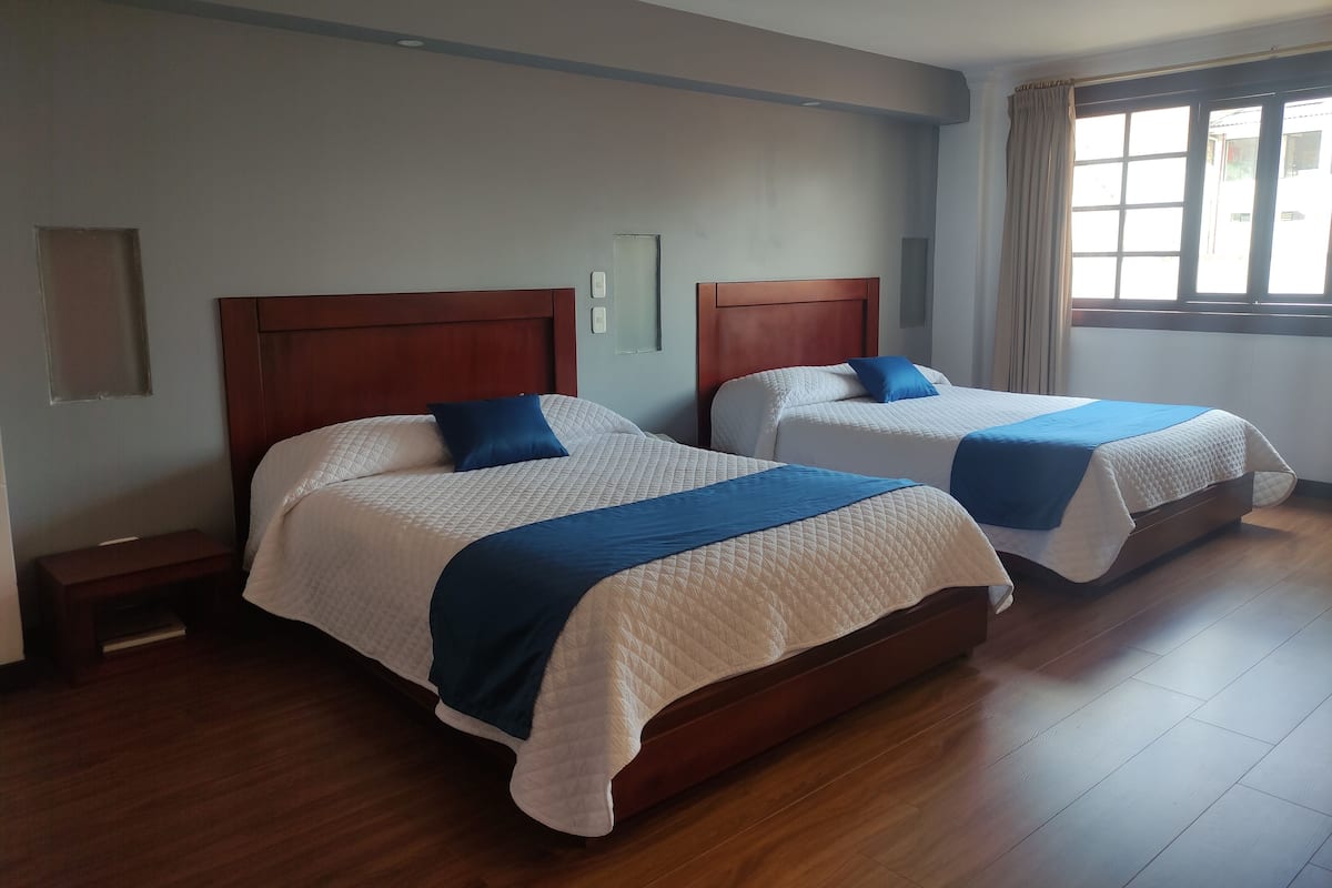 A hotel room with two beds, wooden headboards, and a large window with curtains.