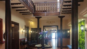A spacious lobby with a tiled floor, a central table with flowers, a staircase, and a seating area with blue cushions. - SÁ Hotel (Cuenca)