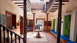 A hotel lobby with a central round table, a staircase with wooden railings, and a green wall with climbing plants. - SÁ Hotel (Cuenca)