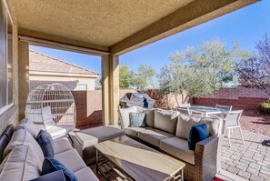 Un espacio de patio cubierto con mobiliario exterior, que incluye un sofá, sillas y una mesa.