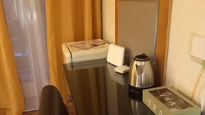 Una camera d'albergo con pavimento in legno, una poltrona in pelle nera, un tavolino con un dispositivo bianco, un bollitore d'argento e un libro rilegato intitolato “TEA”.