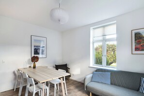 A modern room with a dining table, white chairs, a grey sofa, and a large window with a view of greenery.
