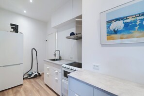 A modern kitchen with white cabinetry, a built-in oven, a sink, and a vacuum cleaner.