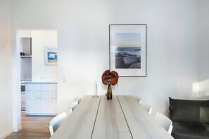 A dining area with a wooden table, white chairs, a vase with flowers, and framed pictures on the wall.