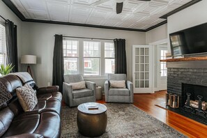 A living room with a leather sofa, two armchairs, a coffee table, a fireplace, and a TV.