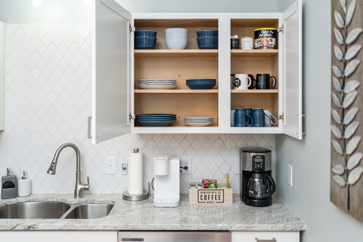 Een keuken met een dubbele spoelbak, een witte betegelde achterwand, een koffiezetapparaat, en een kast met blauw en wit servies.