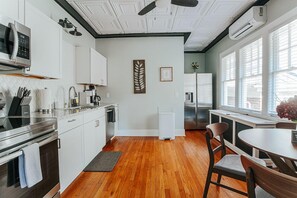 A modern kitchen with white cabinets, stainless steel appliances, and a wooden floor.