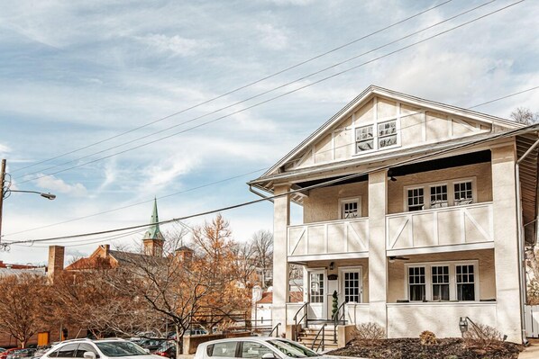 A two-story building with a balcony on the upper floor, a garage on the ground floor, and a visible church steeple in the background.