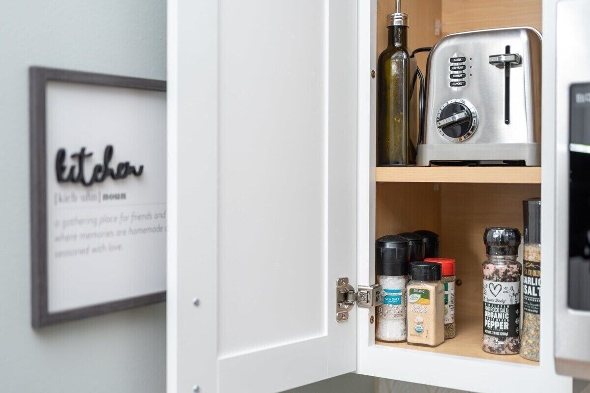A kitchen cabinet with a toaster and various spices.