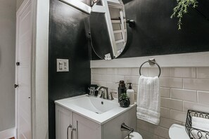 A bathroom with a white sink, black and white tiled walls, a white towel rack, and a small potted plant.