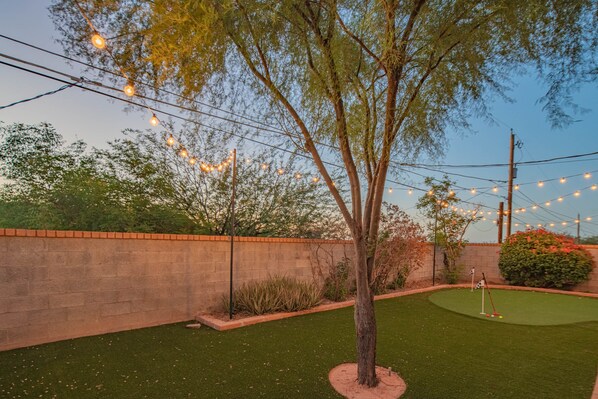 A backyard with artificial lighting, a putting green, and a brick wall.