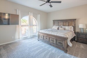 A bedroom with a large bed, a ceiling fan, a TV, a nightstand, and a window with curtains. - NEW! Hidden mini movie theater, Game room, Putt putt, Pool, & MORE (Phoenix)