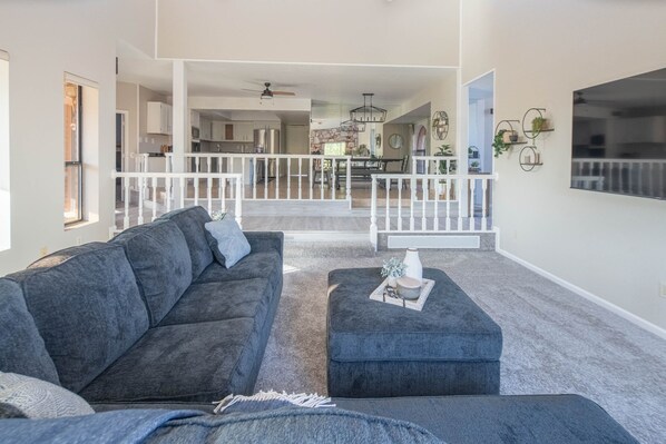 A spacious living area with a grey sofa, ottoman, and a dining table in the background.