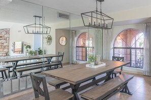 A dining area with a long wooden table, benches, and hanging pendant lights.