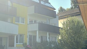 Ein mehrstöckiges Wohngebäude mit flachem Dach, Balkonen und einem gepflegten Garten.