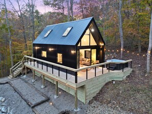 A cabin with a deck, a hot tub, and a staircase leading to the entrance. - Rocky Falls | Hocking Hills, Modern Cabin, Hot Tub (Rockbridge)