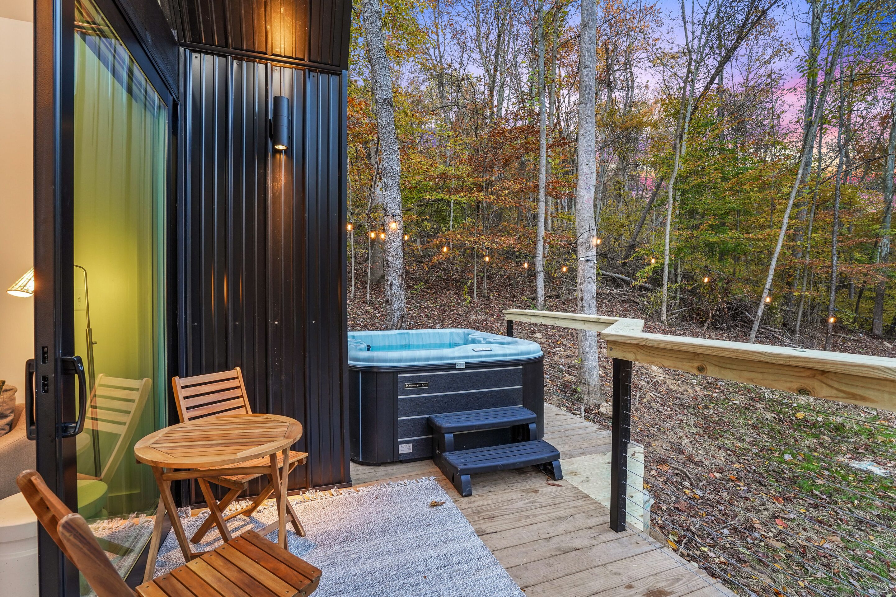 Een houten terras met een jacuzzi, een tafel en stoelen.