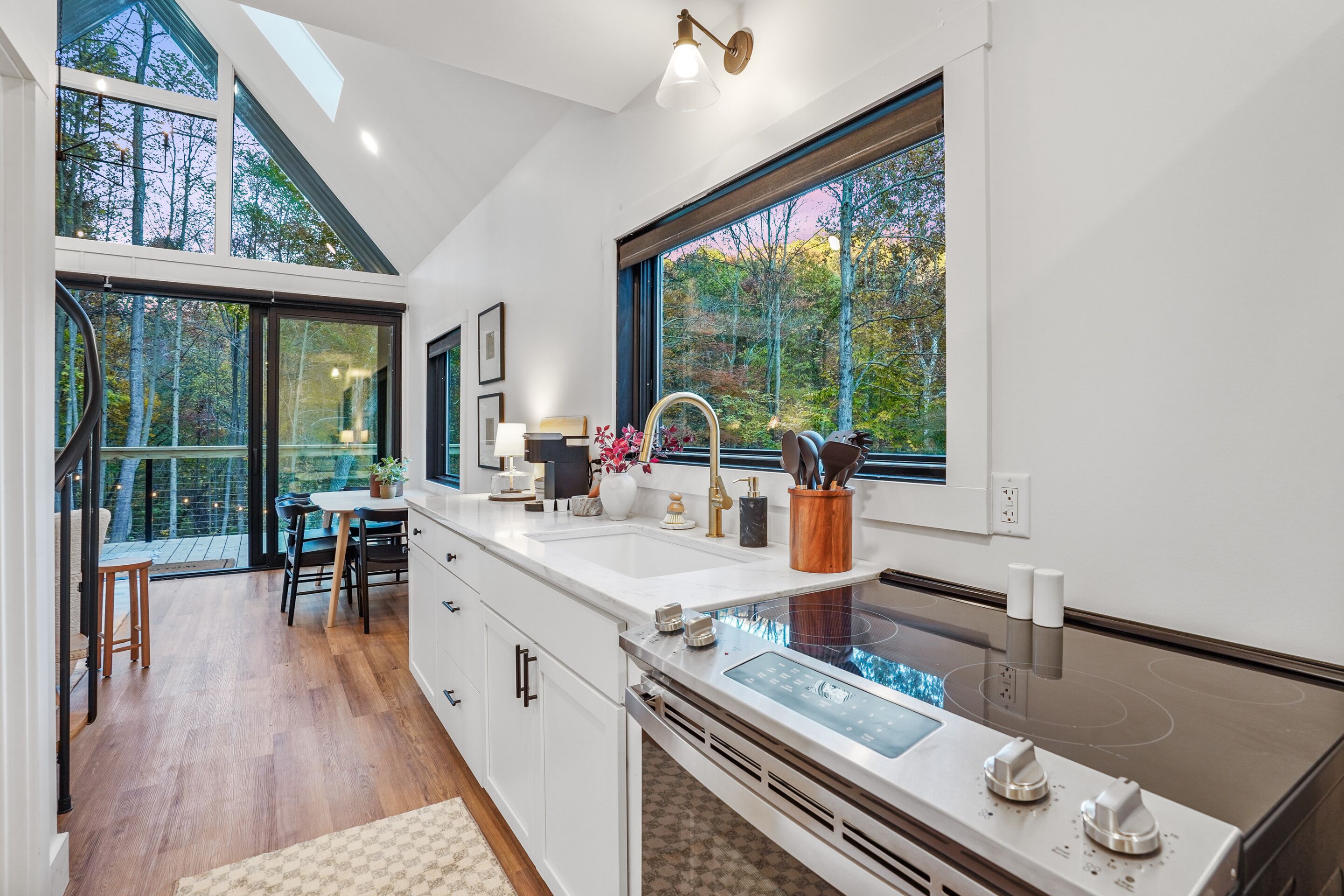 A modern kitchen with a large island, built-in appliances, and large windows offering views of a forested area.