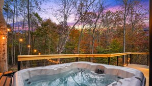Ein Whirlpool mit Holzterrasse und Geländer, umgeben von Bäumen mit Herbstlaub.