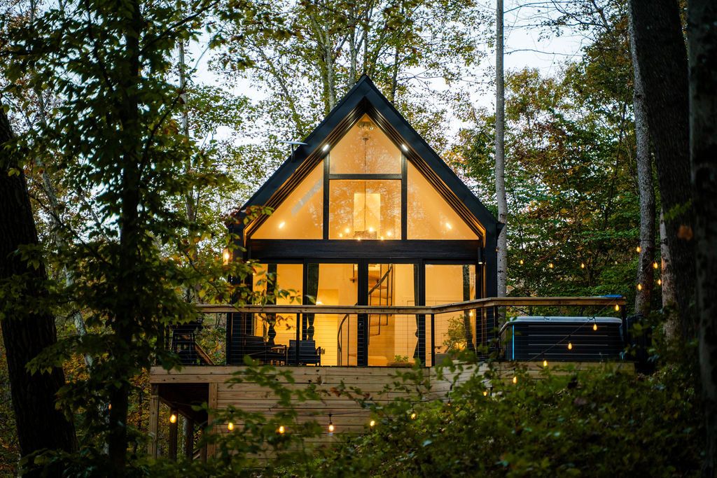 A cabin with a wooden deck, large windows, and a staircase leading to the entrance.
