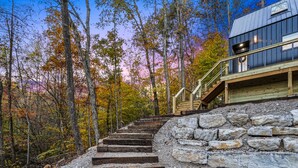 Eine Treppe führt zu einer Holzdielen-Terrasse, an einer Seite eine Steinmauer und an der anderen Seite ein Metallgebäude.