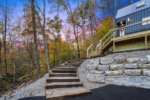 A staircase leading to a wooden deck with a stone wall, surrounded by trees with autumn foliage.
