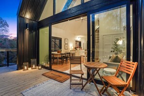 A modern interior with a wooden deck, a dining area with a table and chairs, and a kitchen visible through glass doors. - Rocky Falls | Hocking Hills, Modern Cabin, Hot Tub (Rockbridge)