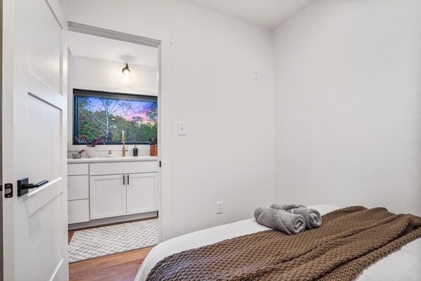 Une chambre à coucher avec un lit, une fenêtre donnant sur des arbres, un lavabo et un miroir.