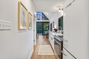 Une cuisine moderne dotée d’un four encastré, un coin repas avec une table et des chaises, et une vue sur les arbres grâce à de grandes fenêtres.