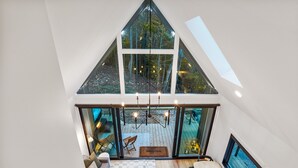 Ein modernes Loft mit schrägen Wänden, großen Fenstern und Blick auf ein bewaldetes Gebiet.