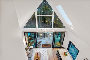 A modern loft-style room with a sloped ceiling, large windows, and a view of a forested area.