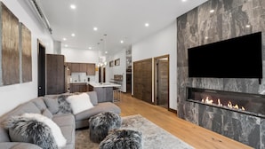Ein modernes Wohnzimmer mit einer Eckcouch, einem Kamin und einer Küche im Hintergrund.