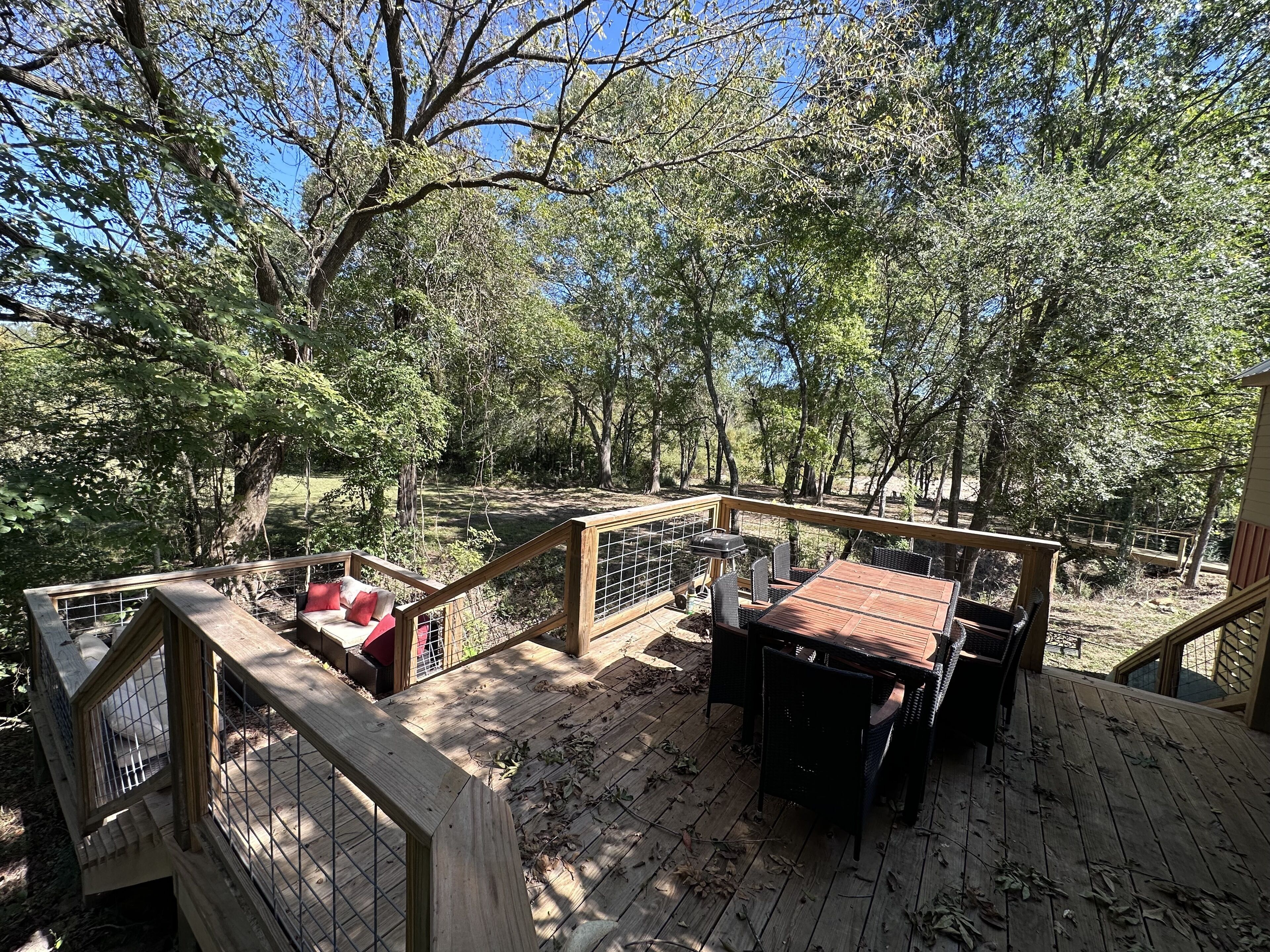 Um deck de madeira com uma mesa e cadeiras, cercado por árvores.