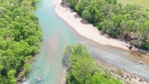 Un río serpentea por una zona boscosa con una playa de arena y un pequeño edificio a lo lejos.
