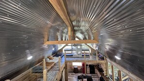 Un interior moderno con techo inclinado, vigas de madera y un espacio central abierto.