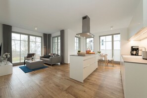 A modern kitchen with a central island, large windows, and a dining area with a table and chairs. - Moderne Ferienwohnung mit Eigener Sauna und Balkon - Villa Pauline Fewo 06 - Villa Pauline (Göhren)