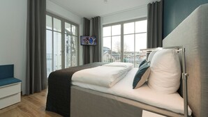 Ein modernes Hotelzimmer mit Bett, Fernseher, großen Fenstern und Blick auf die Stadt.